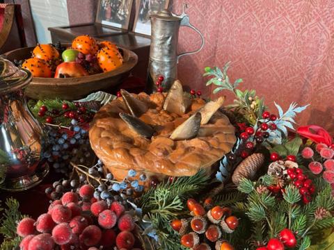 A pastry pie sits in the middle of a Christmas table, surrounded by nuts, fruits and foliage