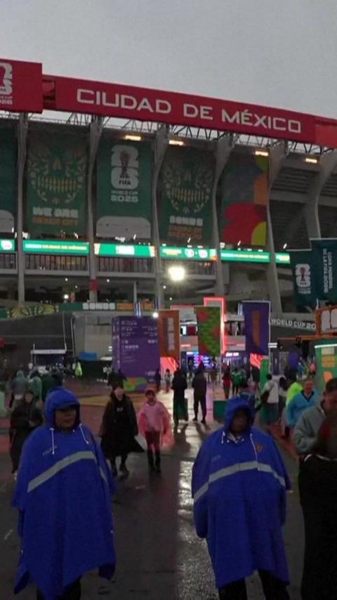 A general view outside Estadio Azteca. People are scattered across the site. The exterior of the stadium is lit up with screens.