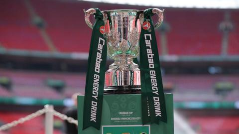The Carabao Cup sits on a plinth with dark green ribbons attached on each handle