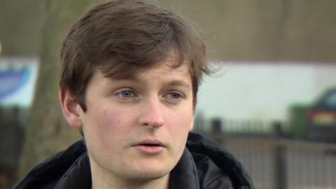 Isaac, who has brown hair with a fringe and is wearing a hooded black coat and a dark green jumper, is pictured in a park