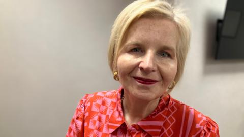 Donna Ockenden looks into camera. She is wearing a patterned red blouse and has short blonde hair.