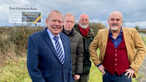 Four men smiling standing on the site of Ross Enterprise park.