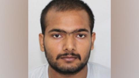 Custody photo of Pankaj Lamba against a grey background. He has dark facial hair, brown eyes and is looking at the camera.