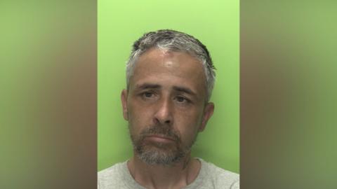 A mugshot of an unshaven man against a green background