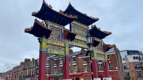 A large decorative red archway marking an entrance to Nelson Street with terraced houses behind, with Chinese restaurants at the bottom of the houses