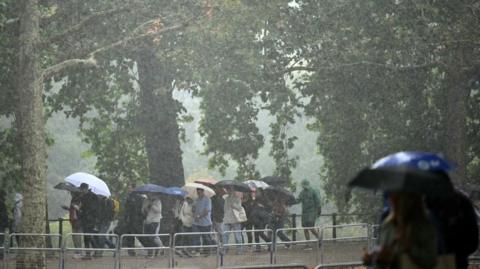 People walk with umbrellas as they're hit by rain and heavy winds