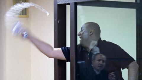 A man behind a glass window is pictured throwing water out of a glass