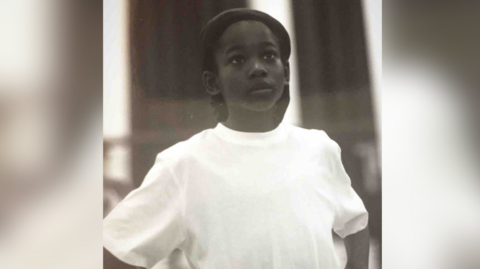 Young boy in white t-shirt looks upwards away from the camera. The photo is black and white.