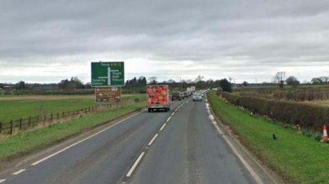 A single lane road with traffic on it. Grass verges on either side and a road sign on the left saying Thirsk A19, Bagby, Balk, Kilburn and Sowerby and Dalton