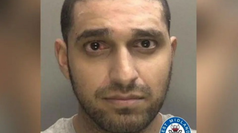 Sharma is pictured in a police mugshot. He has a bloody eye and a grey T-shirt on