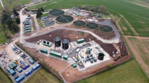 A birds-eye view of the refurbished water recycling centre in Langport. There are round water basins and storage facilities. There is a car park at the edge of the site and around it are green fields.