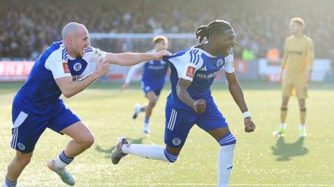 A footballer in a blue kit celebrates scoring a goal