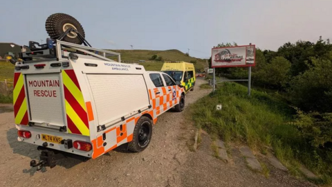 A wide shot of the mountain rescue vehicle parked in front of an ambulance.