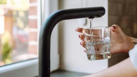 A hand holding a glass under a running tap.