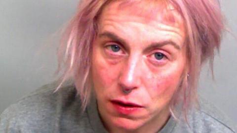 Polly Murphy has a silver nose ring and messy pink hair. She is wearing a grey sweater in this picture taken in police custody.