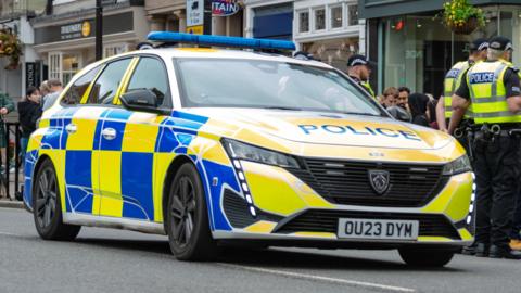 Thames Valley Police car with officers standing to the right hand side of the car.