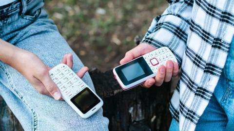 People in jeans hold push-button phones in their hands on their knees - stock photo