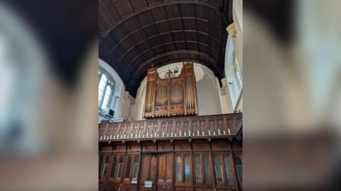 The organ pipes are installed at the back of the chapel, high in the air, above a wooden mezzanine, where the organist would play 