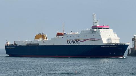 A large commercial vessel, the Commodore Goodwill, heading into a harbour. Skies are blue.