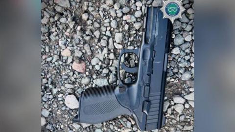 A black airsoft pistol laid flat on a stony ground with the barrel pointing upwards.