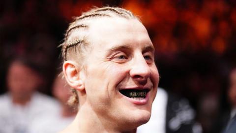 Paddy Pimblett smiles so you can see his mouthguard before a fight, which reads 'men speak up'