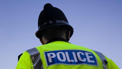 A stock image of a police officer in uniform, including a helmet, photographed from behind