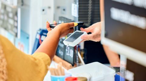 A customer paying at a shop using a mobile phone and contactless card machine.