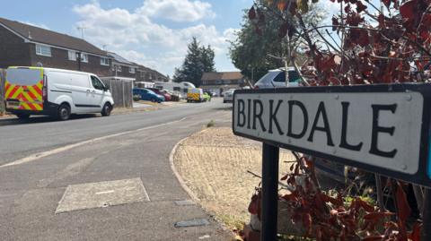 A general view picture of a street sign for Birkdale, with a police van and police car on the left.