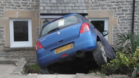 A blue Suzuki Swift crashes into the steps leading to a house.