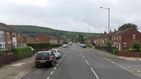 Google Street View image of Birchington Avenue. It is a narrow, two-lane street, with houses on both sides, some cars parked at the side of the road, and street lights spaced out along its length.