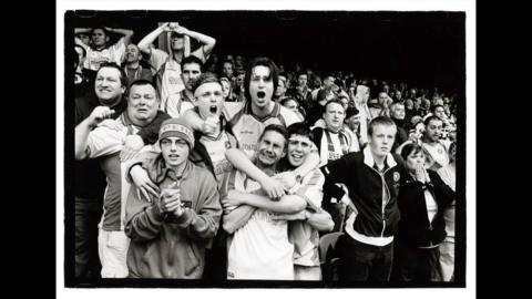 Black and white photograph of Torquay United fans in the away end at Southend United, with anguish on their faces, moments before they are promoted to the old Second Division in 2004.
