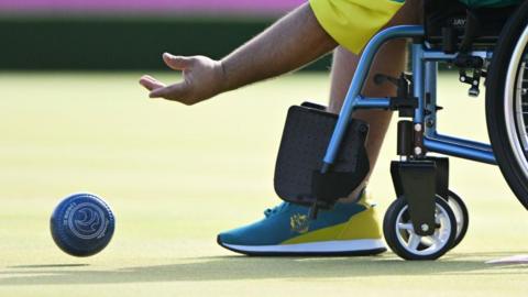 A stock image showing a person in a wheelchair wearing blue and green trainers, rolling a blue ball across green felt.