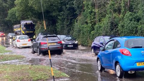 Cars drive through flood water on a busy road. 