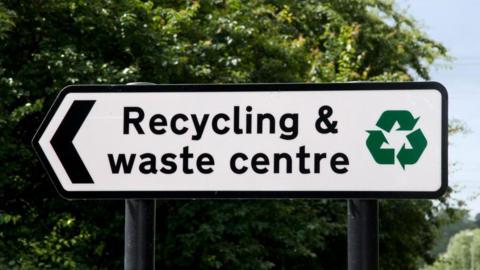 A black and white road sign, which reads 'recycling and waste centre'