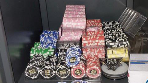 Piles of poker chips of different colours in a safe, along with a triangle "all in" button, on top of a white dealer button, and a pack of cards. 