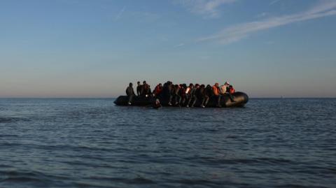 Black inflatable dinghy in the English Channel. It is filled with people. 