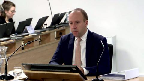 Matt Hancock in blue suit sitting at table with microphone at Covid inquiry