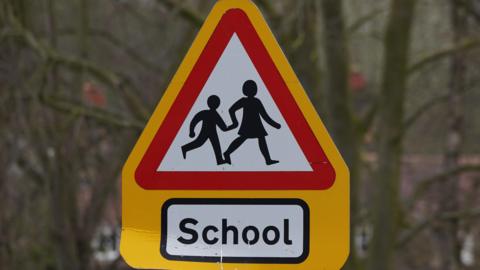 A yellow triangle 'children crossing' sign with 'School' below the sign in black text.