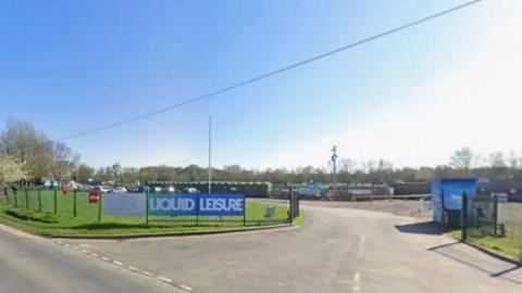 A Google Streetview of a road heading to a car park with a Liquid Leisure sign on a blue hoarding attached to the fence alongside.