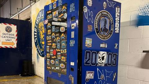 Graffiti covering a blue vending machine at the Croud Meadow football ground.