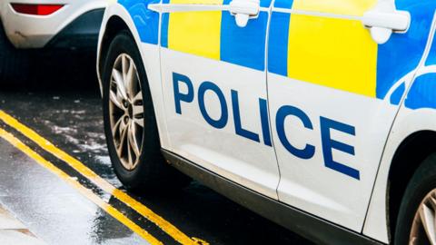 A generic image of a police car in the UK, parked by a double yellow line on a road.