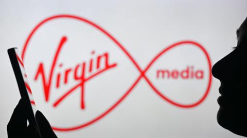 Virgin Media's logo with a silhouetted person in the foreground using a mobile phone.