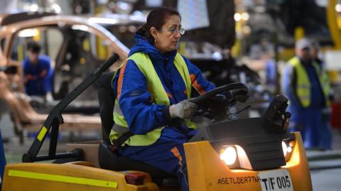 A female warehouse worker driving a factory-floor vehicle