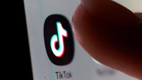 A picture of someone tapping an app. The app has the TikTok logo and says the name of the company below it.
