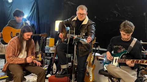 Ryan Durrans, Scott Concepcion, Alex Moore and Matty Murphy from Wigan indie rock band The Lathums stand shoulder to shoulder in a recording studio and smile for a photograph 