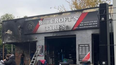 People working outside Beecroft's Tyres Ltd, a shop that shows signs of fire damage