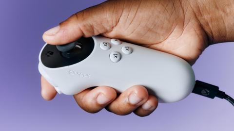 A hand holds a white joystick controller, with four buttons on the top and a joystick controlled by the user's thumb