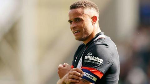 Luton Town captain Carlton Morris smiling as he touches his armband