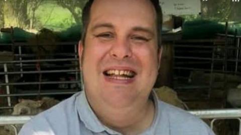 A smiling man wearing a light blue shirt and short brown hair