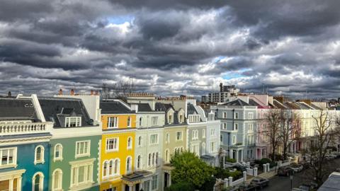 Very dark grey clouds fill the sky over brightly painted London houses